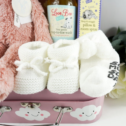 pink baby gift case with white clouds includes a soft pink pig by Happy Horse, soft white knit baby booties with a tie, soft white socks with writing on the sole, white cotton baby hat with two knotted corners, Love boo room and pillow spray, love boo baby wash