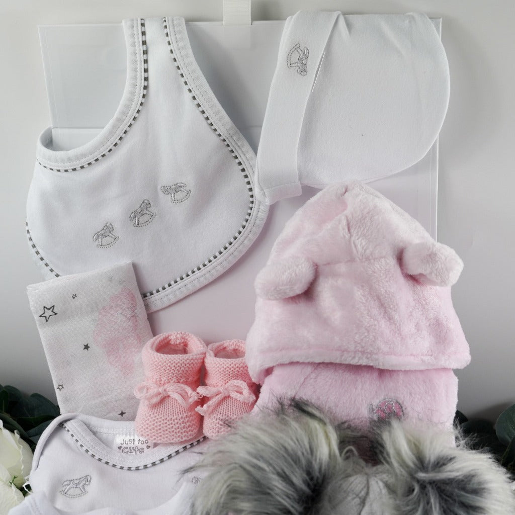 White magnetic hamper box with ribbon tab, include is a white baby layette with silver embroidered rocking horses which includes a baby sleep suit , baby vest., baby mittens, baby hat and baby bib. Pink soft fleece dressing gown with cute ears, pink knit bootis with toies, soft grey and cream fluffy double pom pom hat