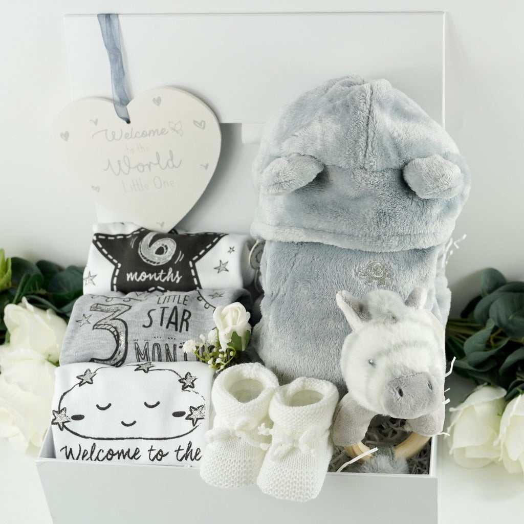 White hamper box with baby milestone vests, newborn, three months and six months size, grey baby dressing gown with cute ears, zebra ring rattle and white baby knit booties