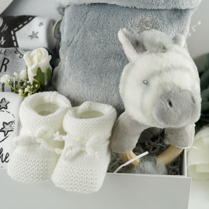 White hamper box with baby milestone vests, newborn, three months and six months size, grey baby dressing gown with cute ears, zebra ring rattle and white baby knit booties