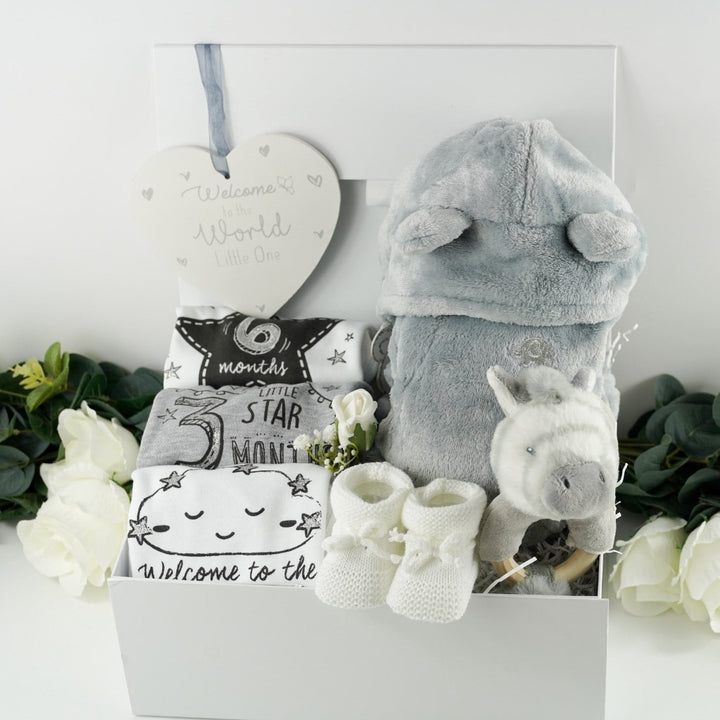 White hamper box with baby milestone vests, newborn, three months and six months size, grey baby dressing gown with cute ears, zebra ring rattle and white baby knit booties