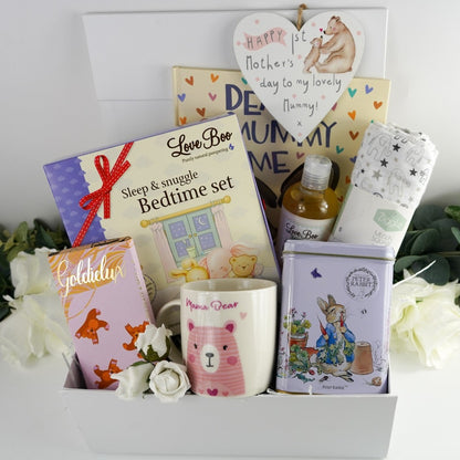 First mothers day girt hamper in a white magnetic hamper box with Love boo natural products for mum and products to help baby sleep, mama bear mug in white with a pink bear, luxury chocolate bar, Peter rabbit cvollectors tin with english breakfast tea bags , white muslin with grey elephants , Dear Mummy love me gift book, Heart shaped hanging plaque with a mummy and baby bear and the writing Happy 1st mothers day