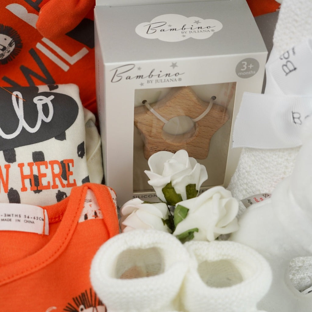 Baby suitcase with 2 bodysuits one orange one cream and grey with matching knot baby hats and bibs, white knit booties, wooden star shaped baby teether, white cotton cellular blanket, white bear rattle
