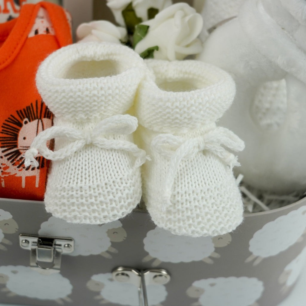 Baby suitcase with 2 bodysuits one orange one cream and grey with matching knot baby hats and bibs, white knit booties, wooden star shaped baby teether, white cotton cellular blanket, white bear rattle