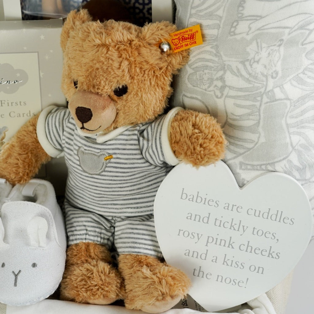 Baby wicker gift hamper, luxury cream baby clothing set with gold angel wings design, camel rubber teether, white baby slippers with animal face, grey and white baby dream blanket, steiff baby teddy in stipe pyjamas, baby milestone cards