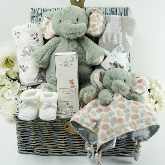 willow hamper basket with baby gifts including soft grey elephant, elephant baby comforter , elephant and giraffe baby swaddle , baby white booties , knitted grey blanket with animals, little Aurelia baby toiletries 