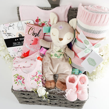 grey hamper basket with a soft fawn lovey with taggies, pink stripe baby blanket heavy weight, baby balck and white book, pink knitted booties, floral baby set, studio chocolate bar