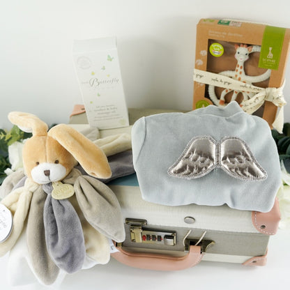 Blue, cream, grey stripe childs keepsake suitcae with luxury baby items including a rabbit comforter in grey, cream and white, sophie la giraffe teether, Luxury grey cashmere mix baby cardigan, baby passport holder and luggae tag in white with a silver plated teddy, velour baby sleepsuit with angel wings in silver, organic baby toiletries
