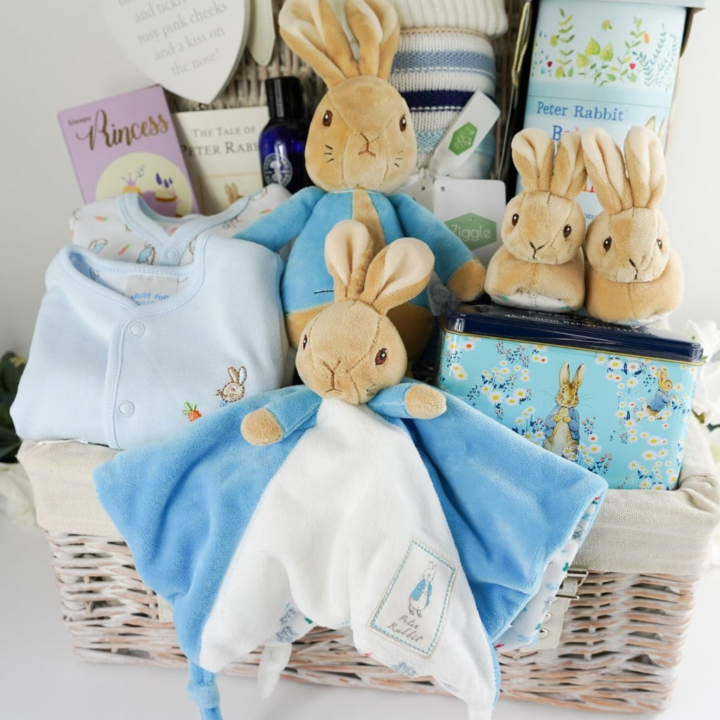 Luxury baby hamper with Peter rabbit itmes including Peter Rabbit soft toy, Peter rabbit baby comforter in blue and white, Soft brown Peter Rabbit baby slippers, Peter Rabbit Time Capsule, Peter Rabbit Book, Peter Rabbit baby clothing set including a pale blue jacket with Peter Rabbit embroidered, Luxury chocolate bar, collectors Peter Rabbit tin with breakfast tea, Soft blue and beige stripe heavy knit baby blanket, Neals yard baby toiletries