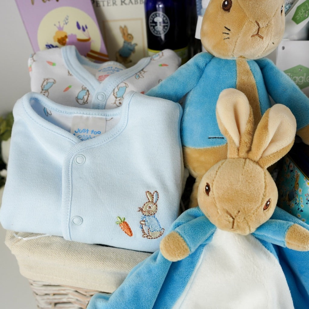 Luxury baby hamper with Peter rabbit itmes including Peter Rabbit soft toy, Peter rabbit baby comforter in blue and white, Soft brown Peter Rabbit baby slippers, Peter Rabbit Time Capsule, Peter Rabbit Book, Peter Rabbit baby clothing set including a pale blue jacket with Peter Rabbit embroidered, Luxury chocolate bar, collectors Peter Rabbit tin with breakfast tea, Soft blue and beige stripe heavy knit baby blanket, Neals yard baby toiletries