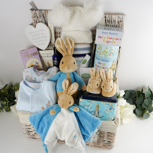 Luxury baby hamper with Peter rabbit itmes including Peter Rabbit soft toy, Peter rabbit baby comforter in blue and white, Soft brown Peter Rabbit baby slippers, Peter Rabbit Time Capsule, Peter Rabbit Book, Peter Rabbit baby clothing set including a pale blue jacket with Peter Rabbit embroidered, Luxury chocolate bar, collectors Peter Rabbit tin with breakfast tea, Soft blue and beige stripe heavy knit baby blanket, Neals yard baby toiletries 