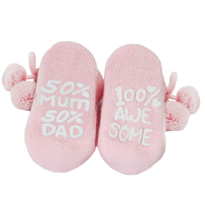 Pink baby socks with pom poms and writing on the sole