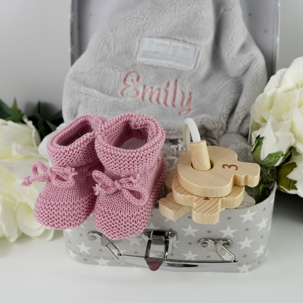 Small baby case with soft grey duck comforter, dusky pink knitted booties, wooden keys on a rope for teething