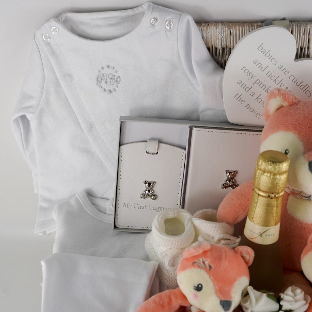 hamper basket with 3 piece baby clothing set, white pu leather baby's firts passport and luggage labels, Friexenet alcohol free fizz, baby soft fox toy, comforter and rattle, booties and white nursery plaque